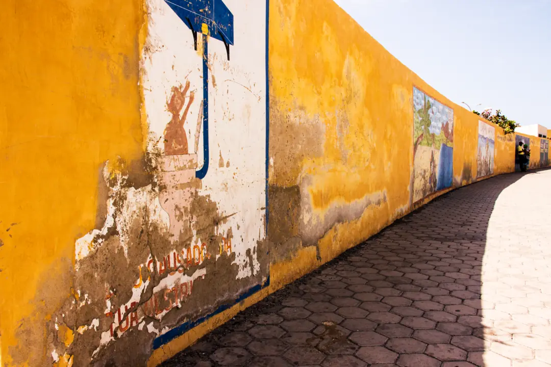 Sunlit yellow wall with murals along a street in Mindelo